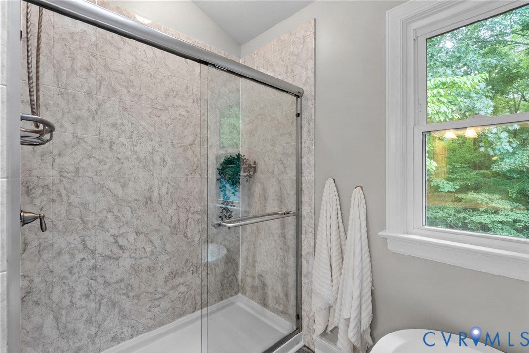 Glass-enclosed shower with stone-look wall panels and brushed nickel fixtures