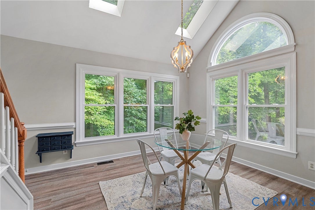 Dining area featuring multiple windows, a large arched window, vaulted ceilings, two skylights, and wood-finish flooring
