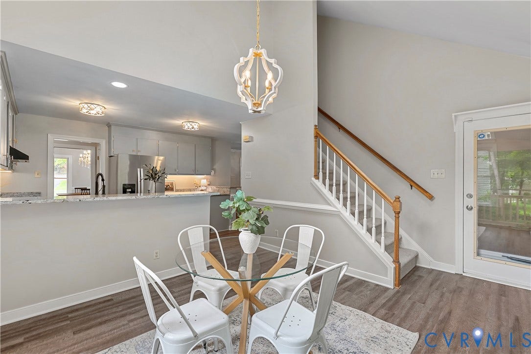 Open-concept living area featuring wood-finish flooring, a contemporary chandelier, and a white-painted staircase with wood handrails