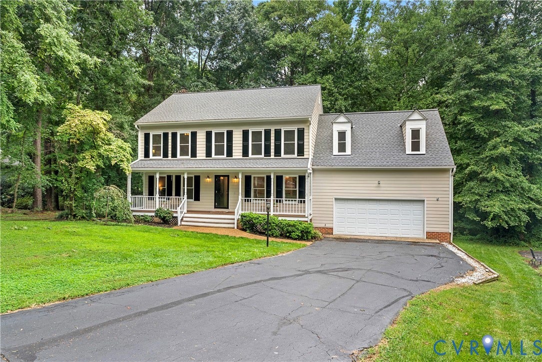 Two-story residence featuring a covered front porch with white railings, a two-car garage with dormer windows, and a paved driveway