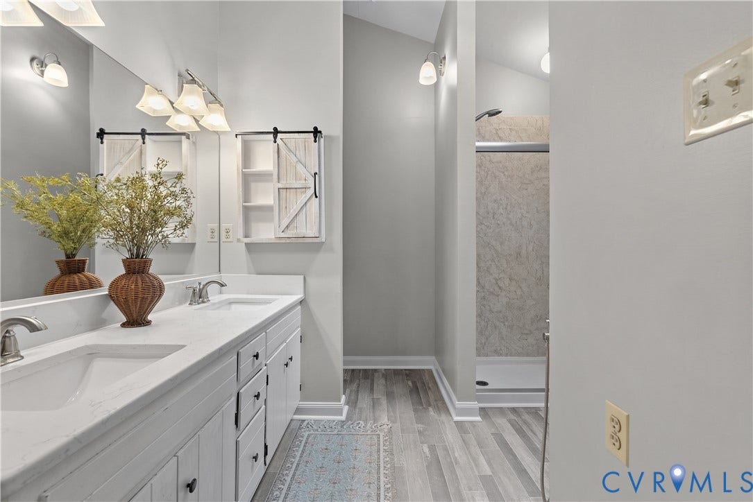 Double vanity with integrated sinks and white cabinetry, complemented by a large mirror and two decorative barn door style wall cabinets