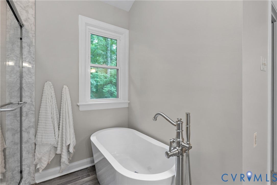 Bathroom featuring a freestanding soaking tub with a floor-mounted brushed nickel faucet, a double-hung window with white trim, and wood-finish flooring