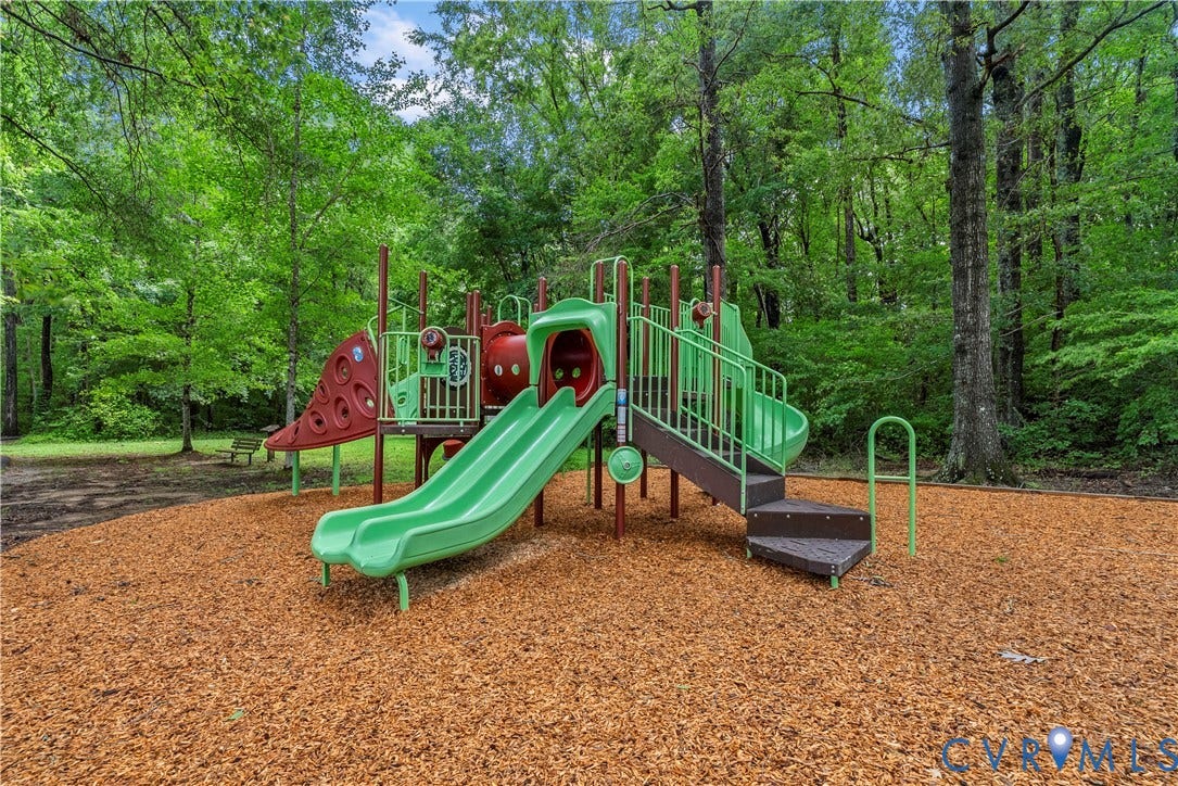 Community playground featuring multiple slides and climbing structures, with a wood chip surface, surrounded by mature trees