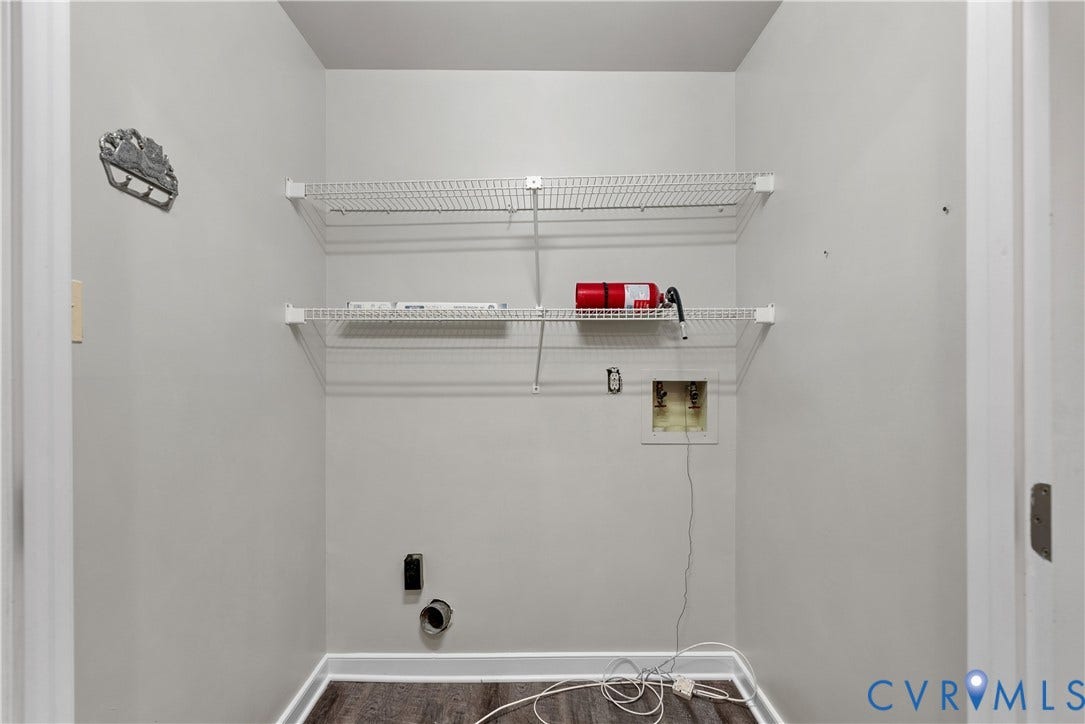 Utility room featuring white wire shelving, light gray walls, dark wood-finish flooring, and white baseboards