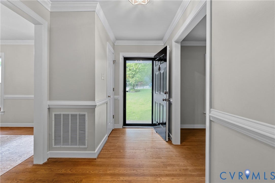Foyer featuring wood-finish flooring, light gray walls, white crown molding, white chair rail molding, and a black paneled front door with a glass storm door