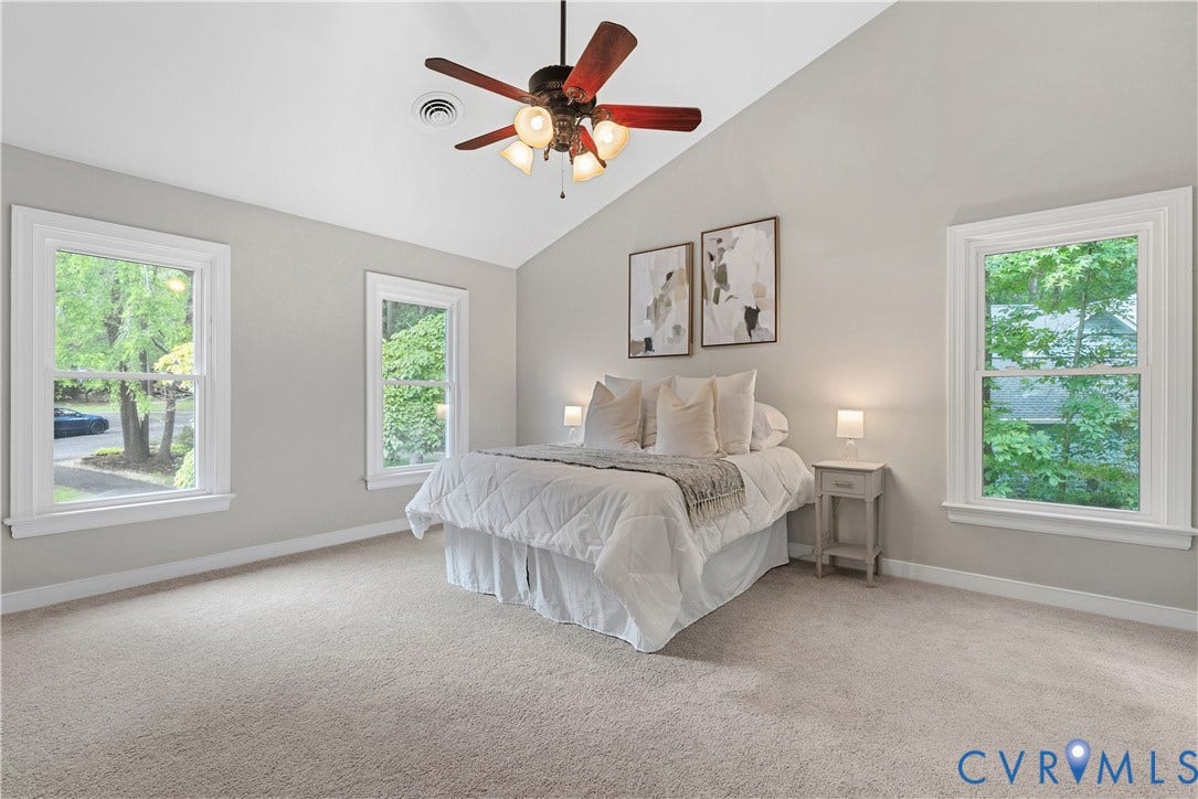 Vaulted ceiling room featuring a ceiling fan with integrated lighting, four double-hung windows, light-toned wall paint, and light-toned carpet flooring