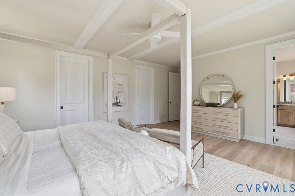 Spacious room featuring wood-finish flooring, an exposed beam ceiling, crown molding, and two panel doors with black hardware