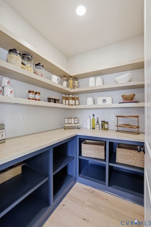 Pantry featuring extensive built-in open shelving, light wood-finish countertops, dark blue base cabinetry, and wood-finish flooring