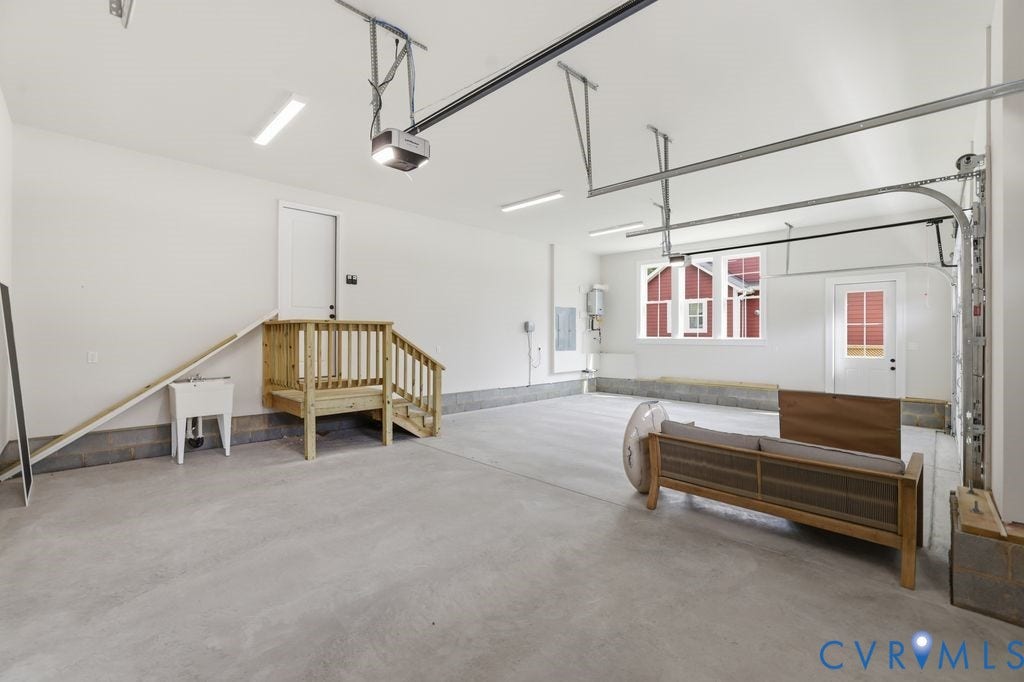 Spacious garage featuring a concrete floor, a utility sink, and a wooden interior staircase with handrails