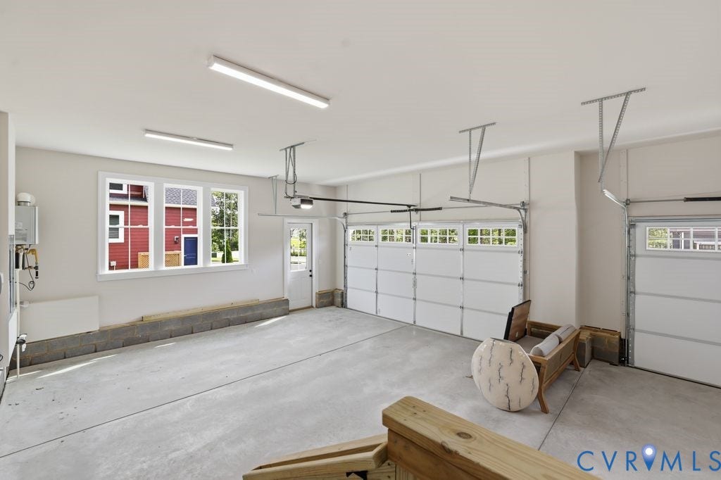 Spacious garage featuring a concrete floor, three white garage doors with upper window panels, and multiple fluorescent light fixtures