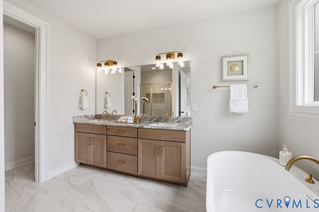 Dual vanity with stone countertop and integrated sinks, under-mount cabinetry, large wall mirror, and gold-finish fixtures