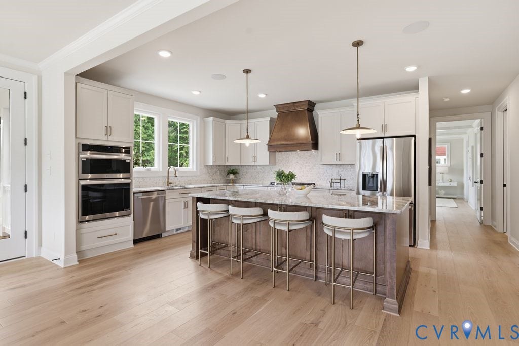 Gourmet kitchen featuring a large island with seating, stainless steel appliances, light wood-finish flooring, white cabinetry, and recessed lighting