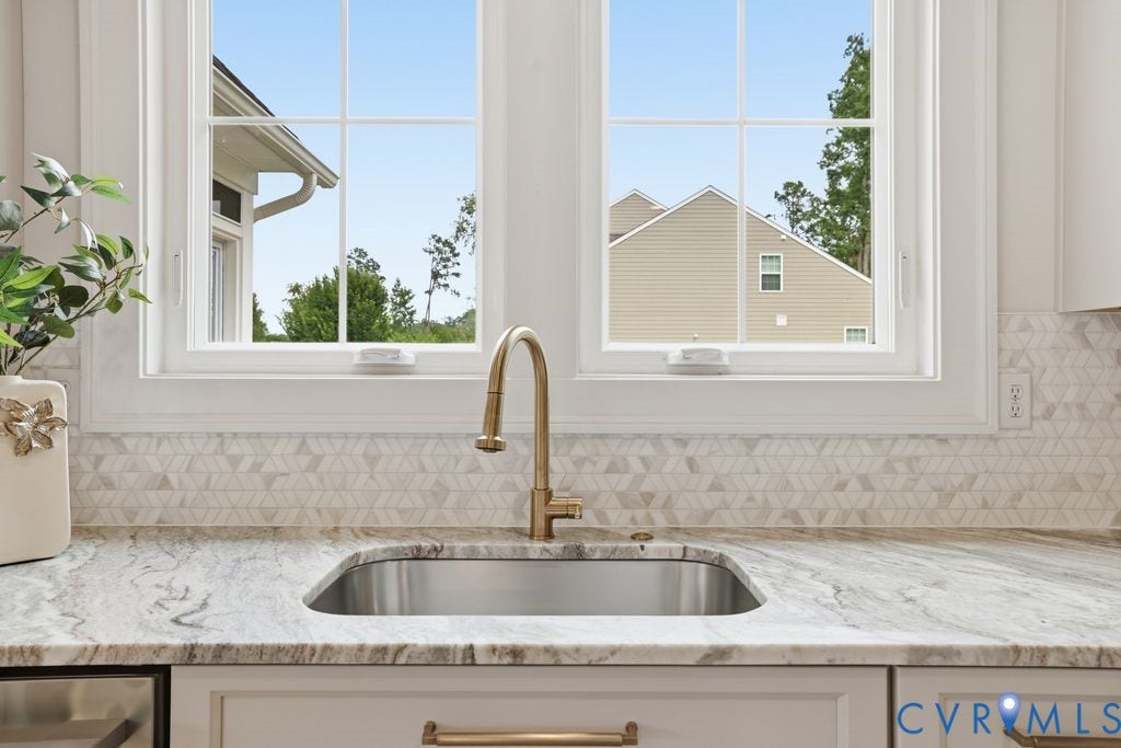 Kitchen sink featuring a brushed brass gooseneck faucet, an undermount stainless steel sink, and a light-toned countertop