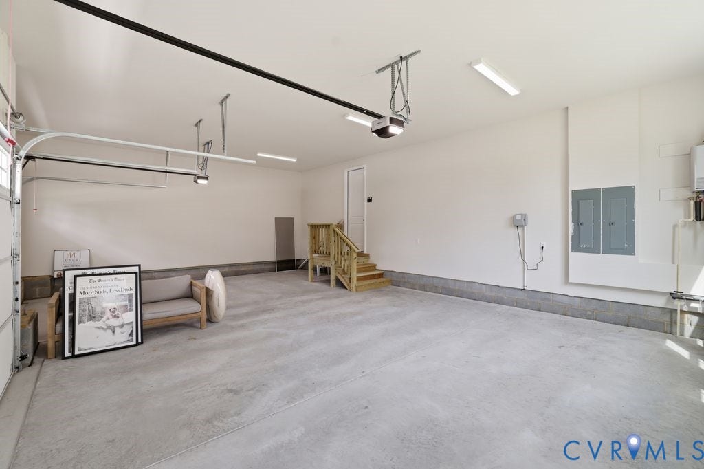Spacious garage featuring a concrete floor, bright overhead lighting, and an interior staircase providing access