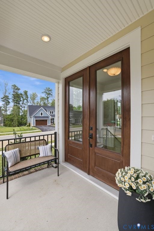 Covered front porch featuring wood-finish double entry doors with clear glass panes, beadboard ceiling with recessed lighting, and durable concrete flooring