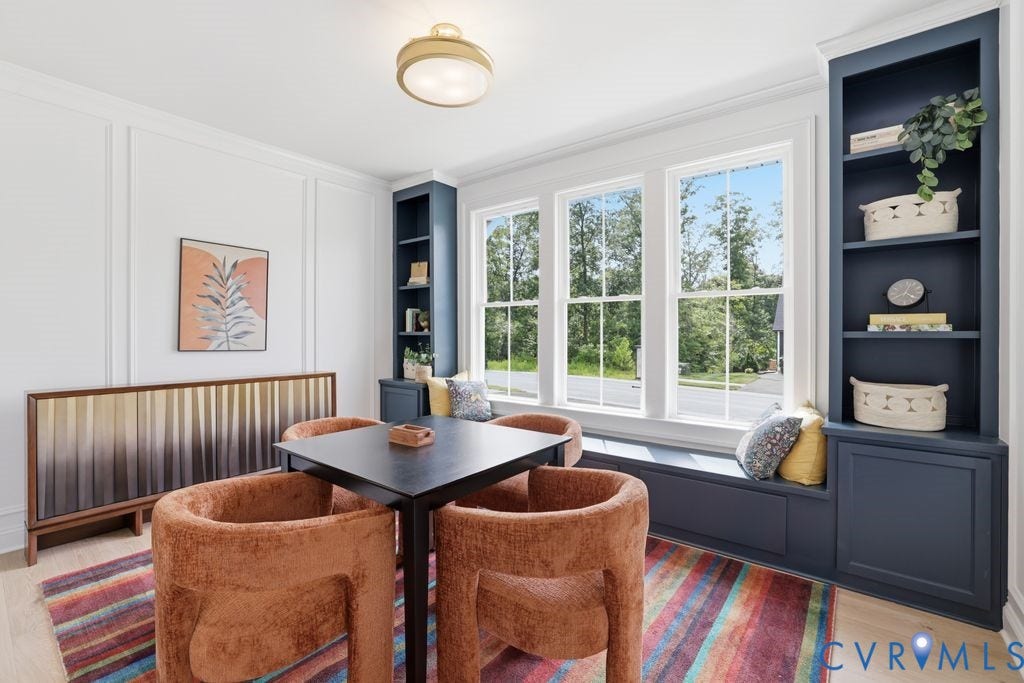 Room featuring a built-in window seat, three large windows, custom built-in shelving, panel molding, and light wood-finish flooring