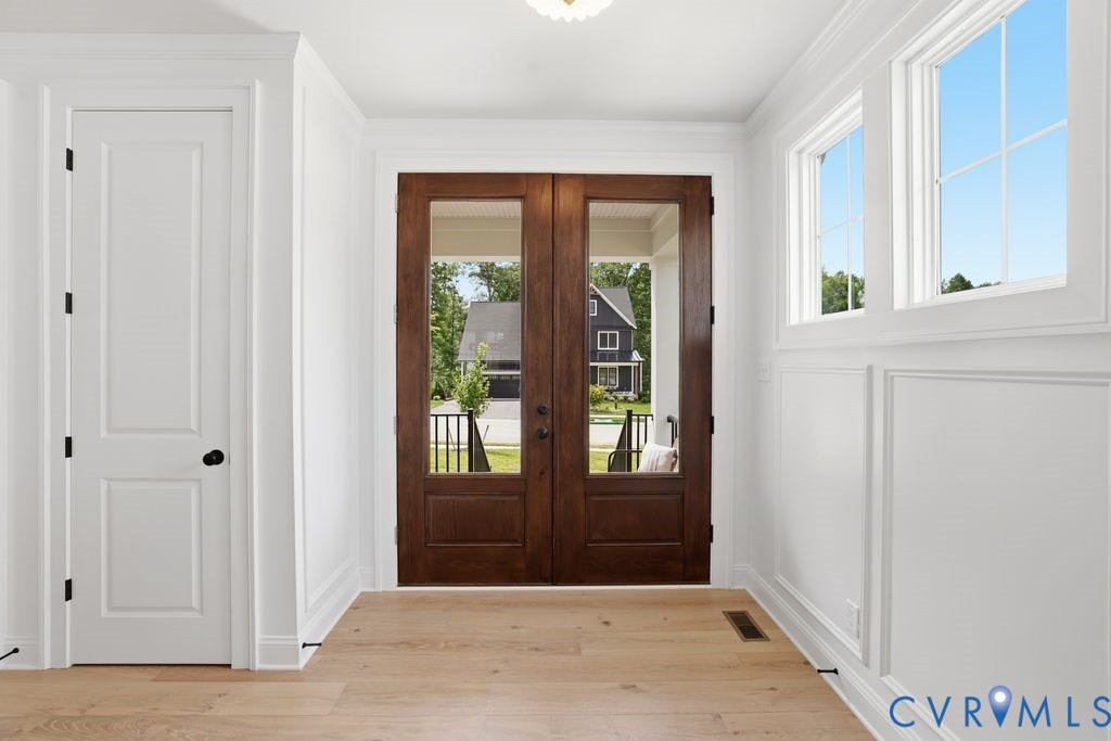 Entryway featuring wide plank wood-finish flooring, a pair of full-light panel doors, white paneled walls, and transom windows