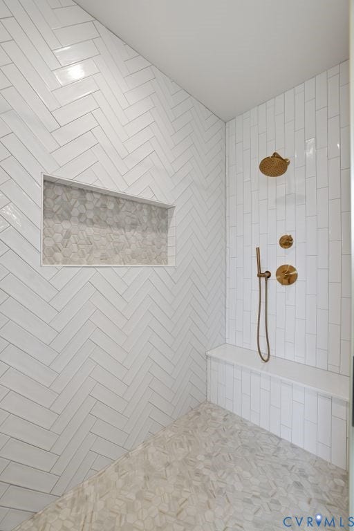 Shower featuring white herringbone wall tile, integrated bench seating, a recessed niche with hexagonal tile, and gold-toned shower fixtures