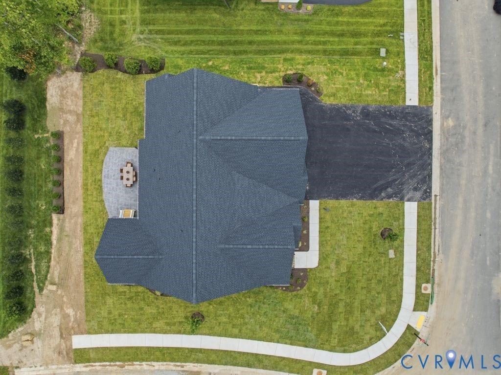 Newly constructed residence featuring an asphalt driveway, a dark gray shingle roof, and an expansive lawn
