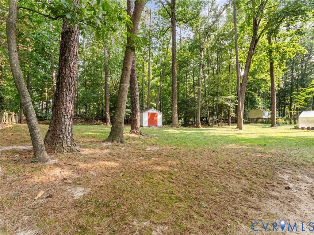 13915 Highpaige Way, Stoney Glen West, Chester, VA 23831 Expansive wooded grounds featuring a white storage shed with a red door, a distinct greenhouse structure, and a secondary yellow shed