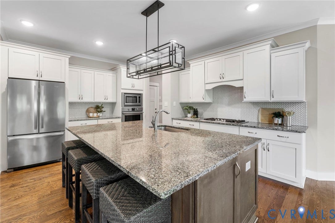 6984 Carden Park Drive, Moseley, VA 23120 Kitchen featuring an oversized large honed granite-topped island with integrated sink, seating and storage, white shaker cabinetry, a herringbone tile backsplash, stainless steel appliances.