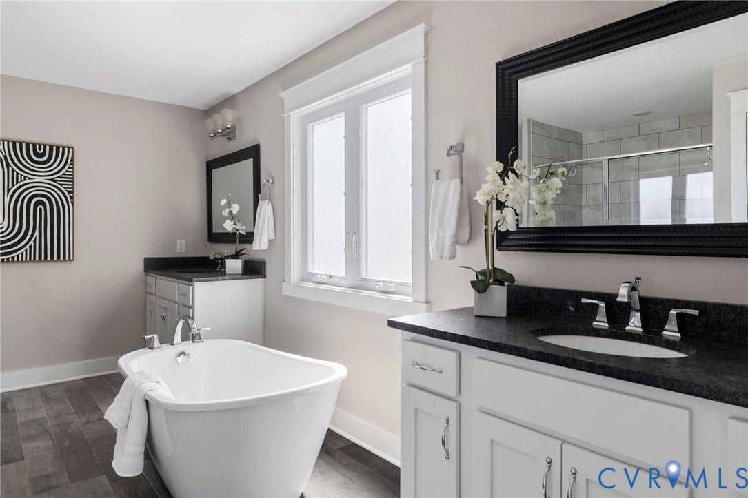 6984 Carden Park Drive, Moseley, VA 23120 Freestanding soaking tub with chrome fixtures, wood-finish flooring, white window trim, and a vanity featuring a dark countertop and undermount sink