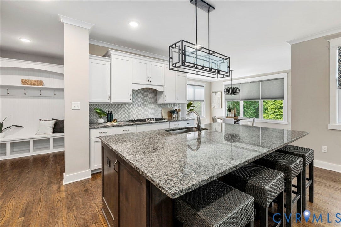 6984 Carden Park Drive, Moseley, VA 23120 Kitchen featuring an oversized large honed granite-topped island with integrated sink, seating and storage, white shaker cabinetry, a herringbone tile backsplash, stainless steel appliances.