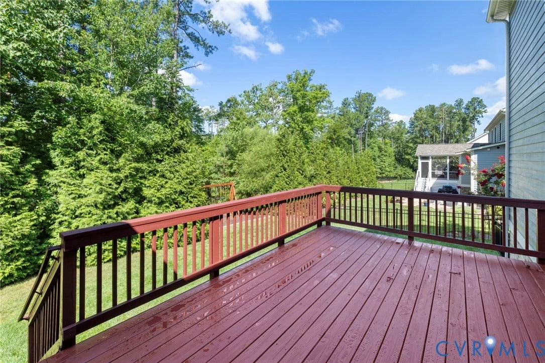 6984 Carden Park Drive, Moseley, VA 23120 Spacious wooden deck featuring a red-stained finish, baluster railing, and lush green landscaping