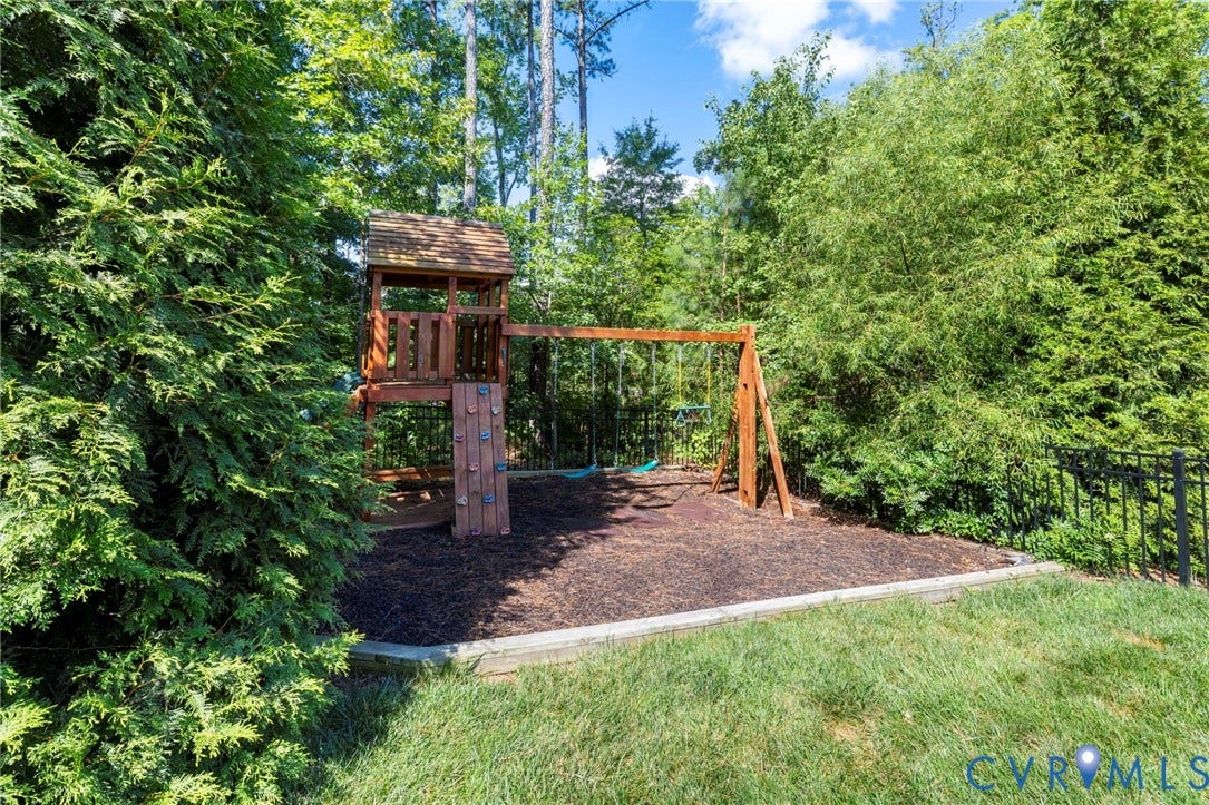 6984 Carden Park Drive, Moseley, VA 23120 Backyard play area featuring a wooden playset with a climbing wall and swings, surrounded by lush trees and a black metal fence