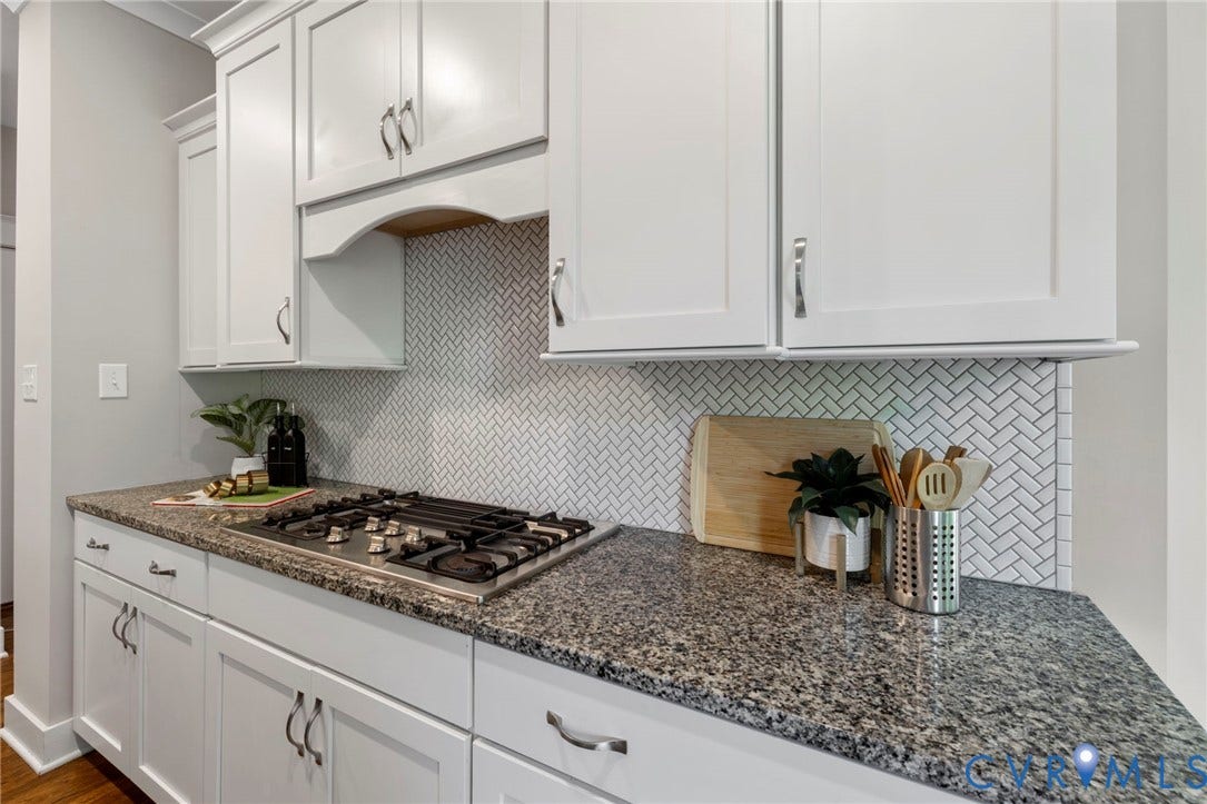 6984 Carden Park Drive, Moseley, VA 23120 Kitchen featuring an oversized large honed granite-topped island with integrated sink, seating and storage, white shaker cabinetry, a herringbone tile backsplash, stainless steel appliances.