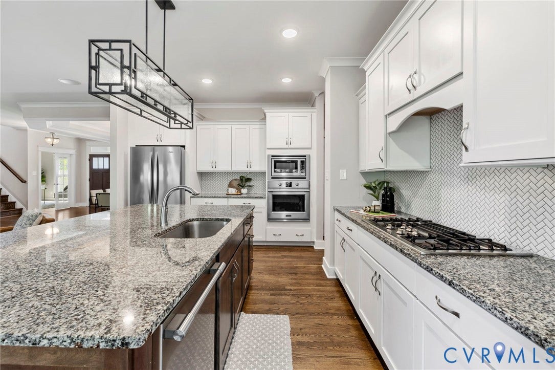 6984 Carden Park Drive, Moseley, VA 23120 Kitchen featuring an oversized large honed granite-topped island with integrated sink, seating and storage, white shaker cabinetry, a herringbone tile backsplash, stainless steel appliances.