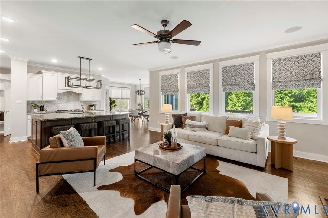 6984 Carden Park Drive, Moseley, VA 23120 Open-concept living area featuring rich wood-finish flooring, a contemporary ceiling fan, and multiple windows with patterned Roman shades