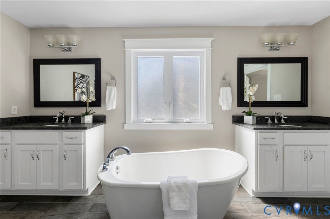 6984 Carden Park Drive, Moseley, VA 23120 Freestanding soaking tub with polished chrome fixtures, flanked by dual vanities featuring white cabinetry, dark countertops, and rectangular mirrors