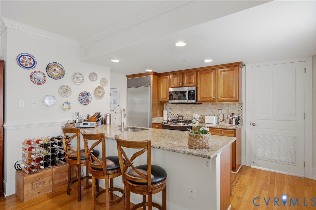 Kitchen featuring a central island with a granite countertop, light wood cabinetry, stainless steel appliances, and wood-finish flooring