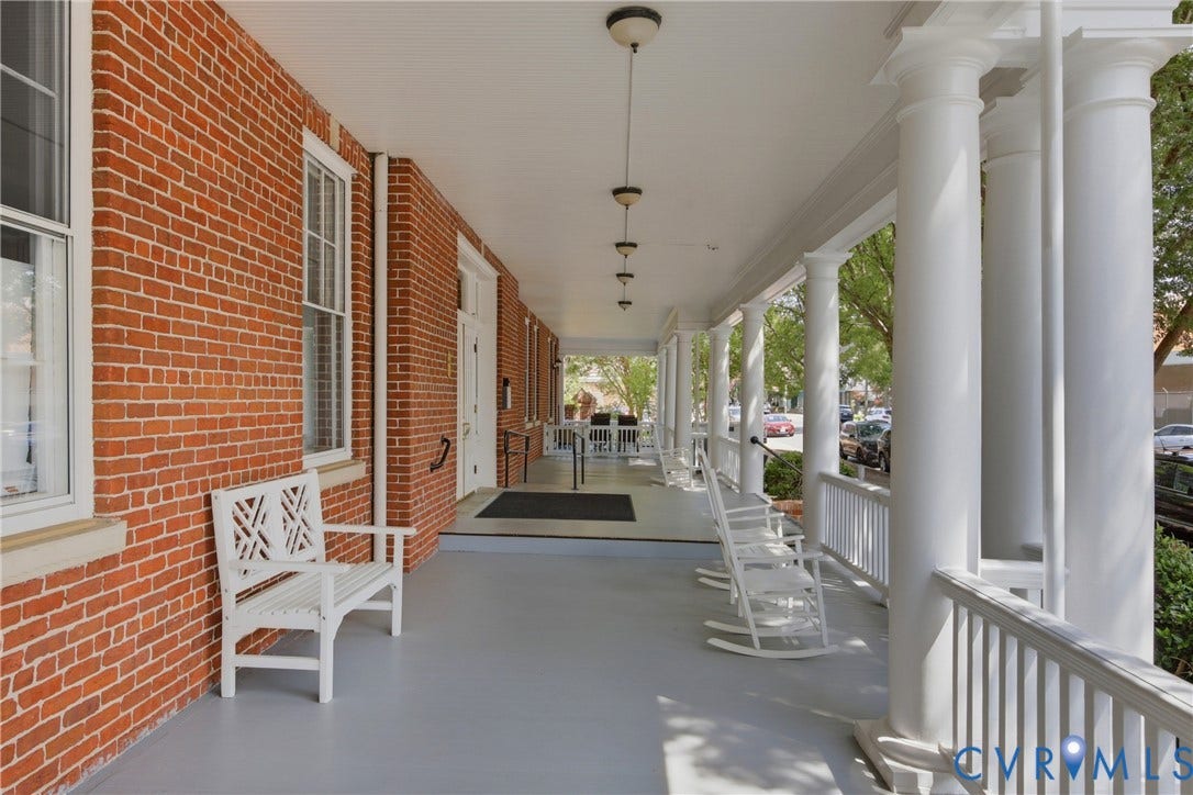 Expansive covered porch featuring a red brick facade, white architectural columns, a light gray painted floor, and recessed lighting fixtures