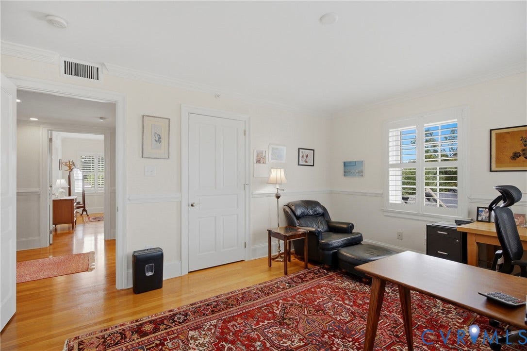 Hardwood flooring extends throughout this room, featuring white paneled wainscoting and a crown molding ceiling