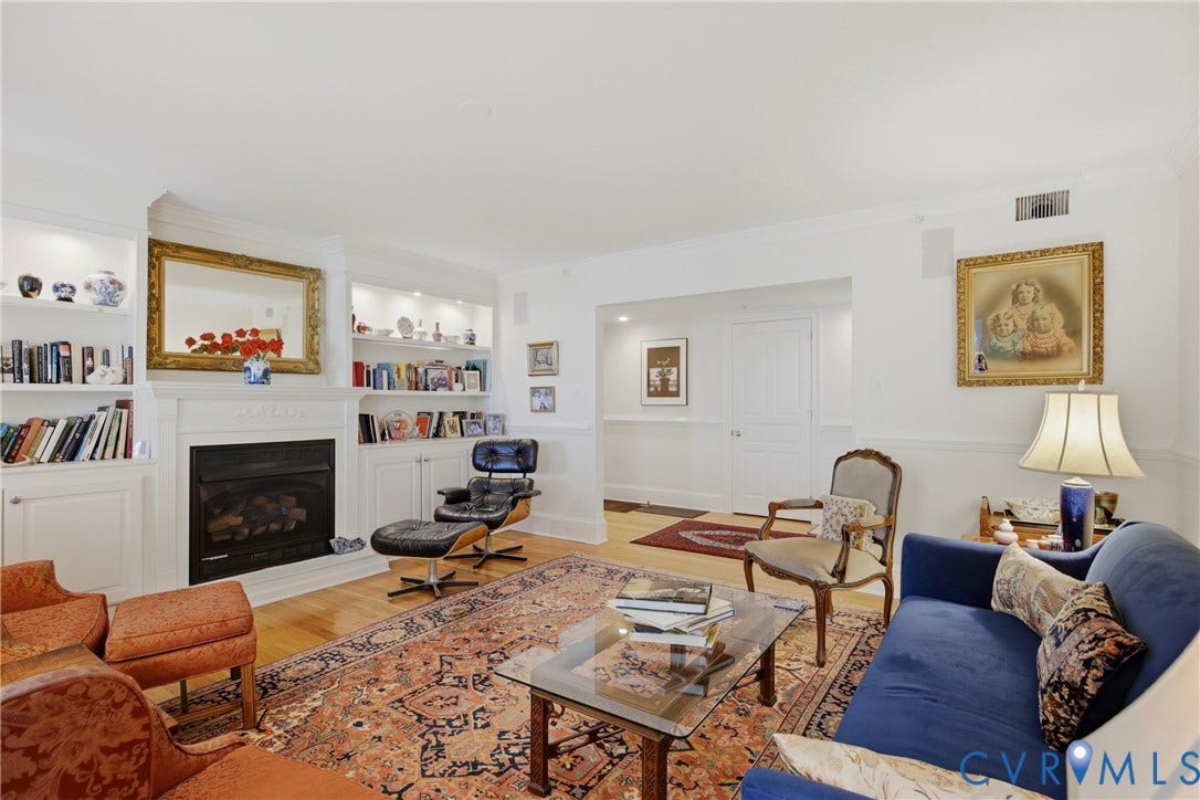 Living area featuring hardwood flooring, a fireplace with a white mantel, and custom built-in shelving with integrated lighting