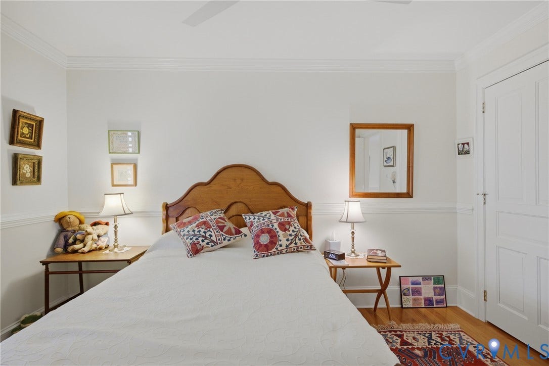 Bedroom featuring a light wood headboard, white walls with wainscoting, crown molding, and wood-finish flooring