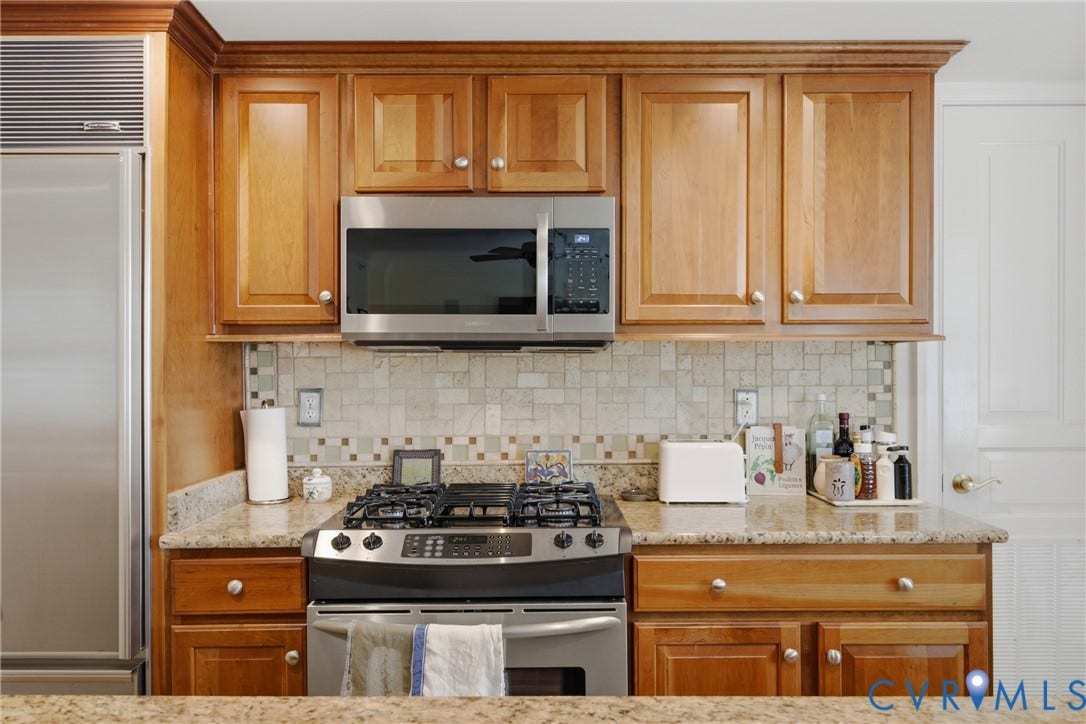 Kitchen featuring wood cabinetry with crown molding, stainless steel appliances including an oven range and microwave, light-toned tiled backsplash, and speckled countertops