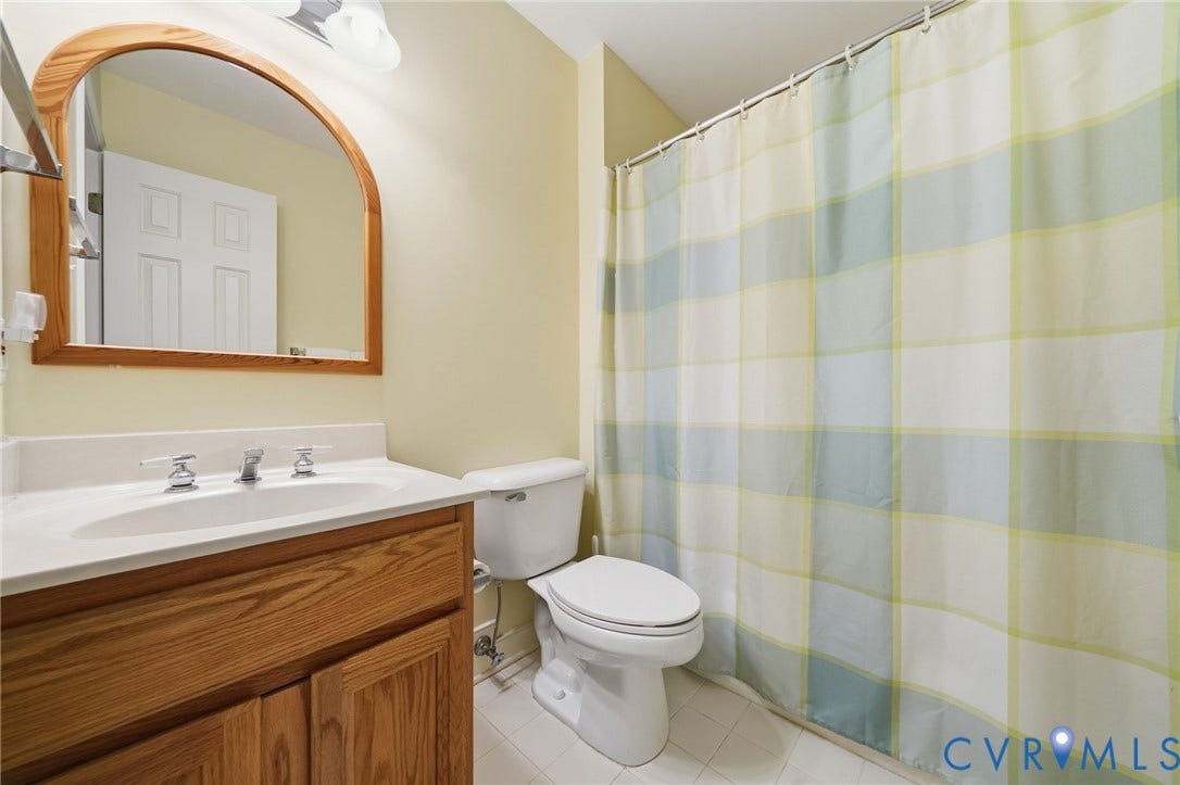 1902 Soldiers Lane, Crozier, VA 23039 Bathroom featuring a wood-finish vanity with an integrated sink and chrome faucet, a wall-mounted arched mirror, a ceramic toilet, and light-toned tile flooring