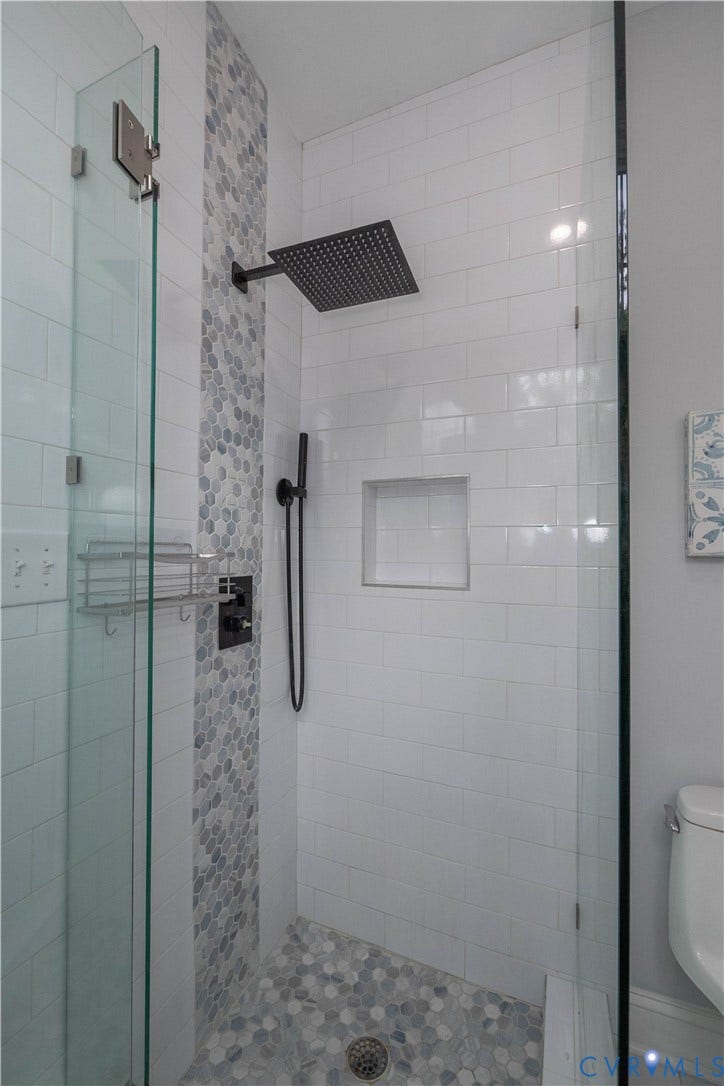 1209 N 22nd Street, Church Hill, Richmond, VA 23223 Walk-in shower featuring a frameless glass enclosure, white subway tile walls, a mosaic tile accent strip, a black rainfall showerhead, and a mosaic tile shower floor