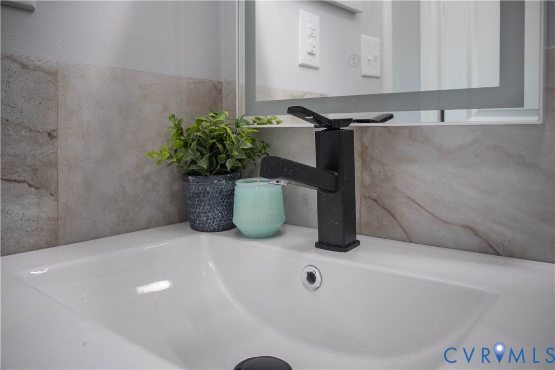 1209 N 22nd Street, Church Hill, Richmond, VA 23223 Integrated white sink with a matte black faucet, complemented by a light-toned stone-look backsplash and an illuminated mirror