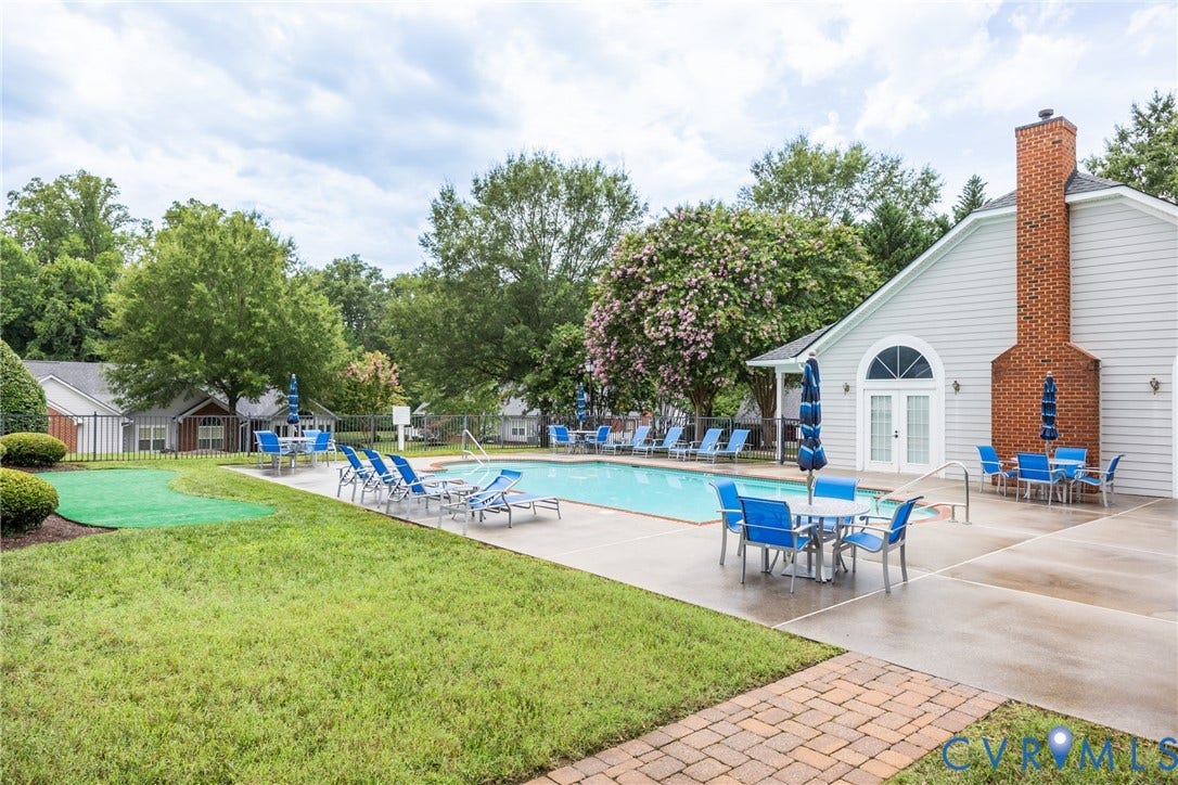 Outdoor swimming pool with surrounding concrete decking, lounge chairs, and dining tables