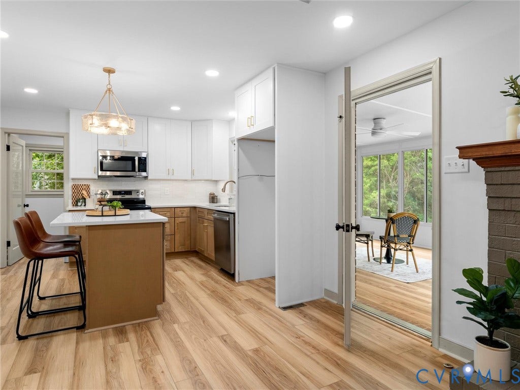 10400 Claybar Trail, Chesterfield, VA 23236 Renovated kitchen featuring wood-finish flooring, a central island with countertop seating, stainless steel appliances, white upper cabinetry, and natural wood lower cabinetry