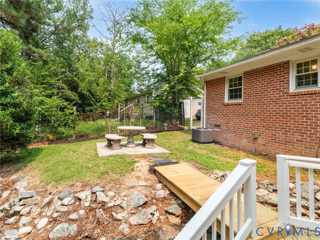 10400 Claybar Trail, Chesterfield, VA 23236 Expansive backyard featuring a red brick exterior, a wooden deck with white railings, and a concrete patio area with a stone table and benches