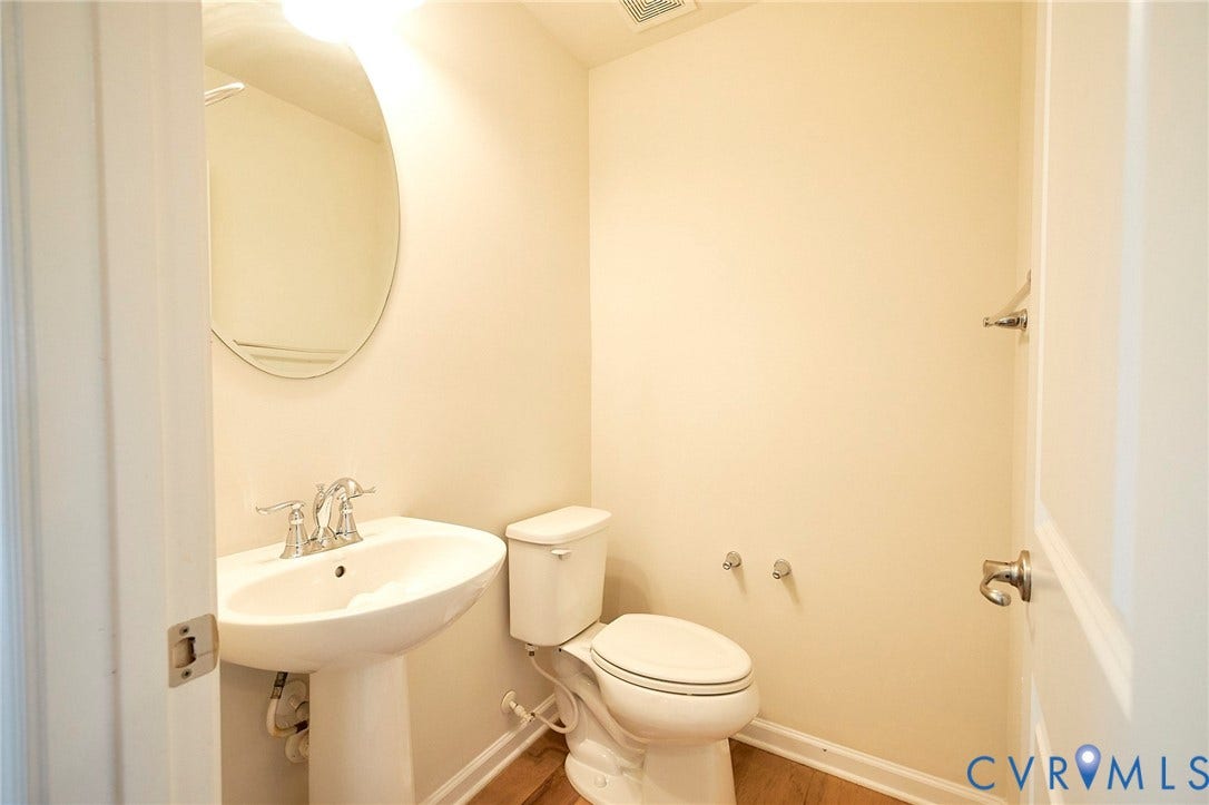 4535 Paxton Glen Court, 3W120, Glen Allen, VA 23059 Pedestal sink with chrome faucet, oval mirror, toilet, and wood-finish flooring