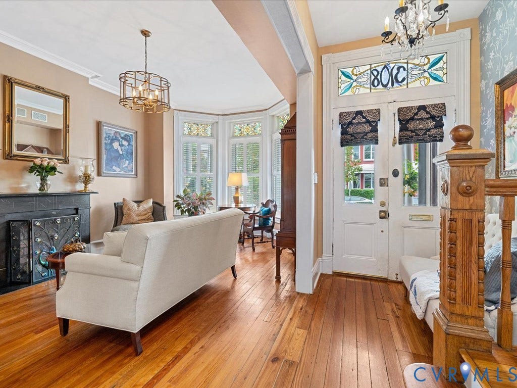 3108 E Broad Street, St John's Historic, Richmond, VA 23223 Entryway and living area featuring wood-finish flooring, an ornate staircase newel post, a transom window with decorative glass, a bay window, and a fireplace with a dark mantel