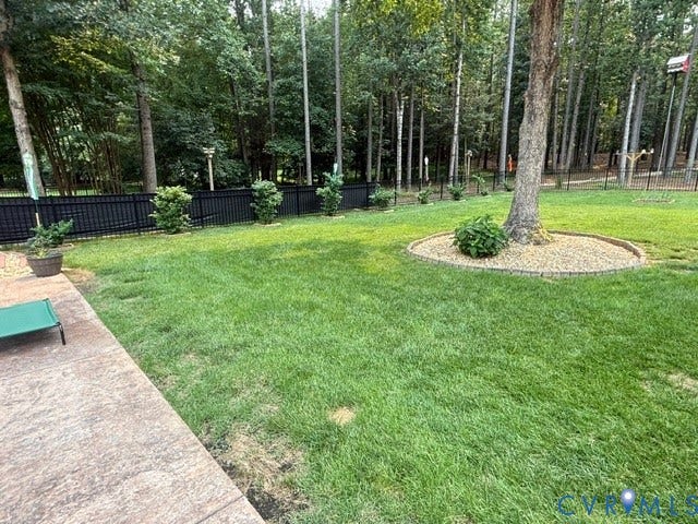 12124 Glen Kilchurn Drive, Chesterfield, VA 23838 Spacious backyard featuring a stamped concrete patio, expansive lawn, decorative black metal fencing, and mature trees providing natural screening