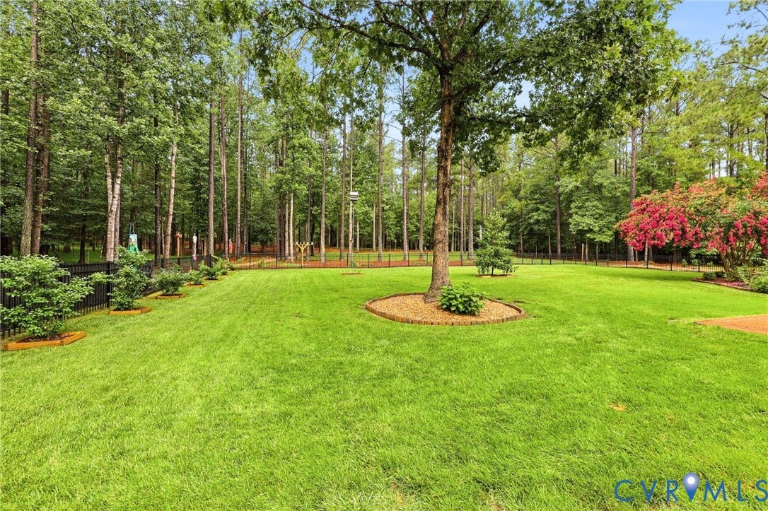 12124 Glen Kilchurn Drive, Chesterfield, VA 23838 Expansive green lawn surrounded by mature trees, featuring a black picket fence and a flowering red tree