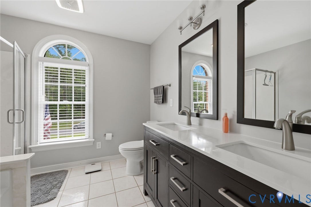 12124 Glen Kilchurn Drive, Chesterfield, VA 23838 Bathroom featuring an arched window with privacy blinds, a dual vanity with a white countertop and rectangular undermount sinks, and a framed mirror